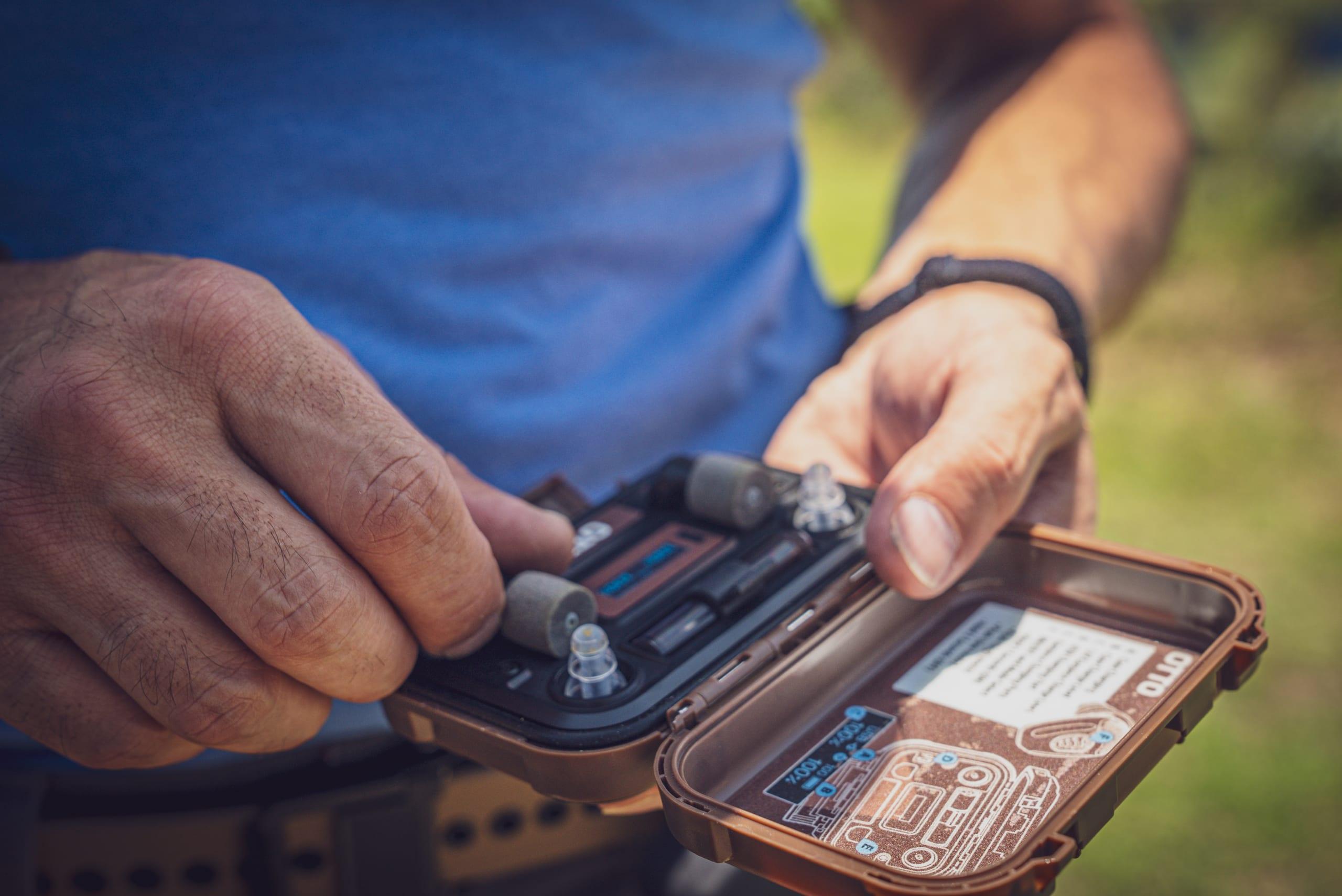 Hands opening a case of electronic earplugs during equipment evaluation