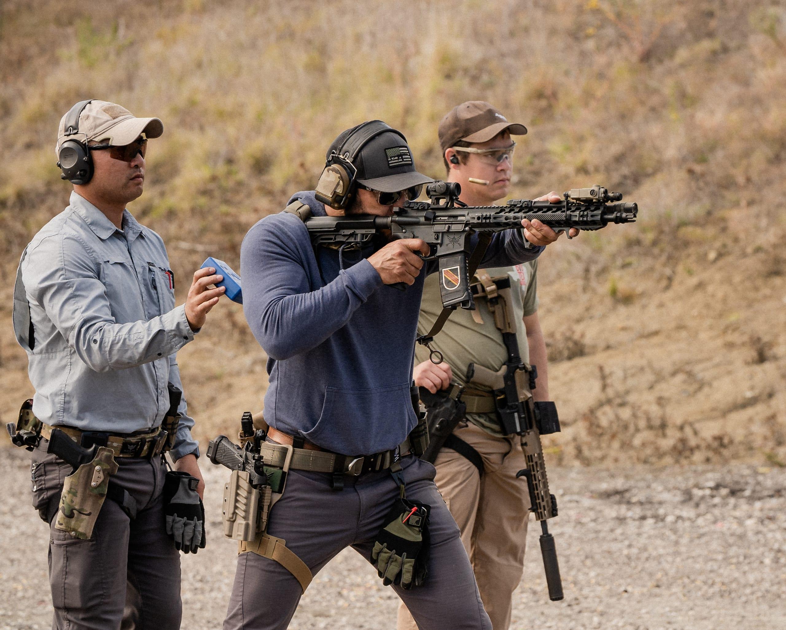 An instructor coaching a shooter running a suppressed carbine on a range