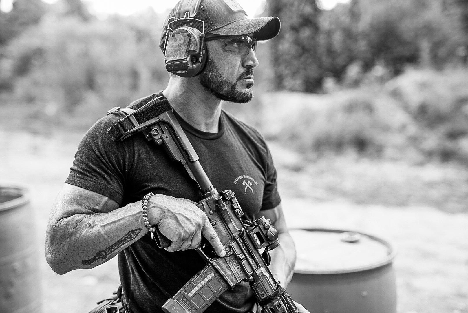 An instructor on the range in ear protection, carrying a braced short-barrelled carbine at the ready